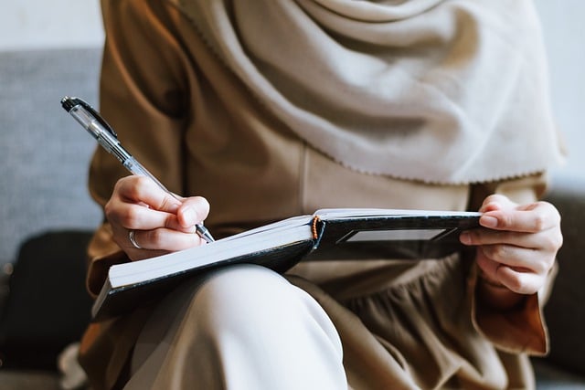 A woman writing in a notebook, resting on her knee.